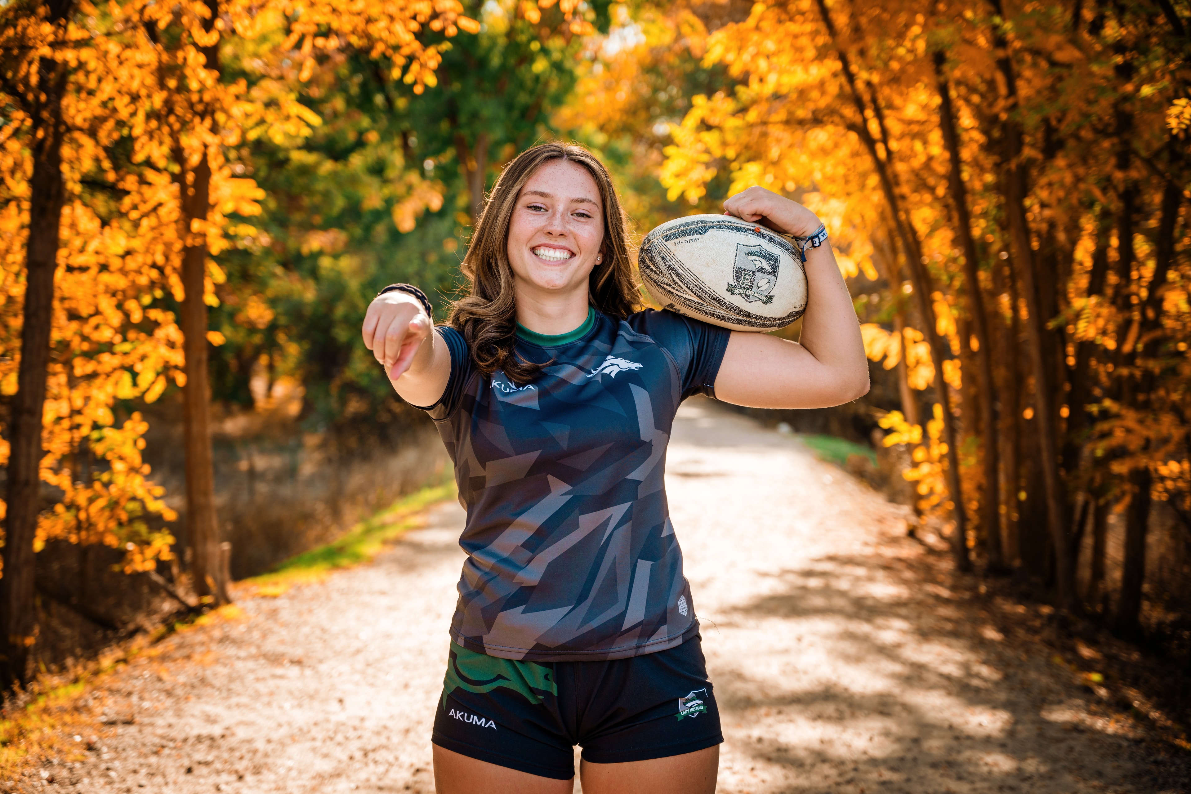 Female rugby player running through autumn forest path — athlete portrait