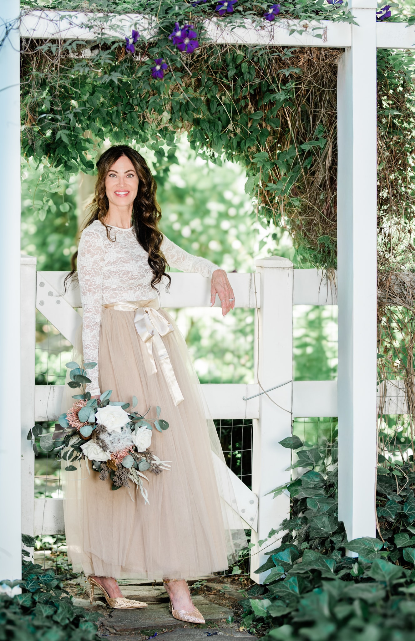 Bride holding bouquet under flowering pergola — Idaho wedding photographer
