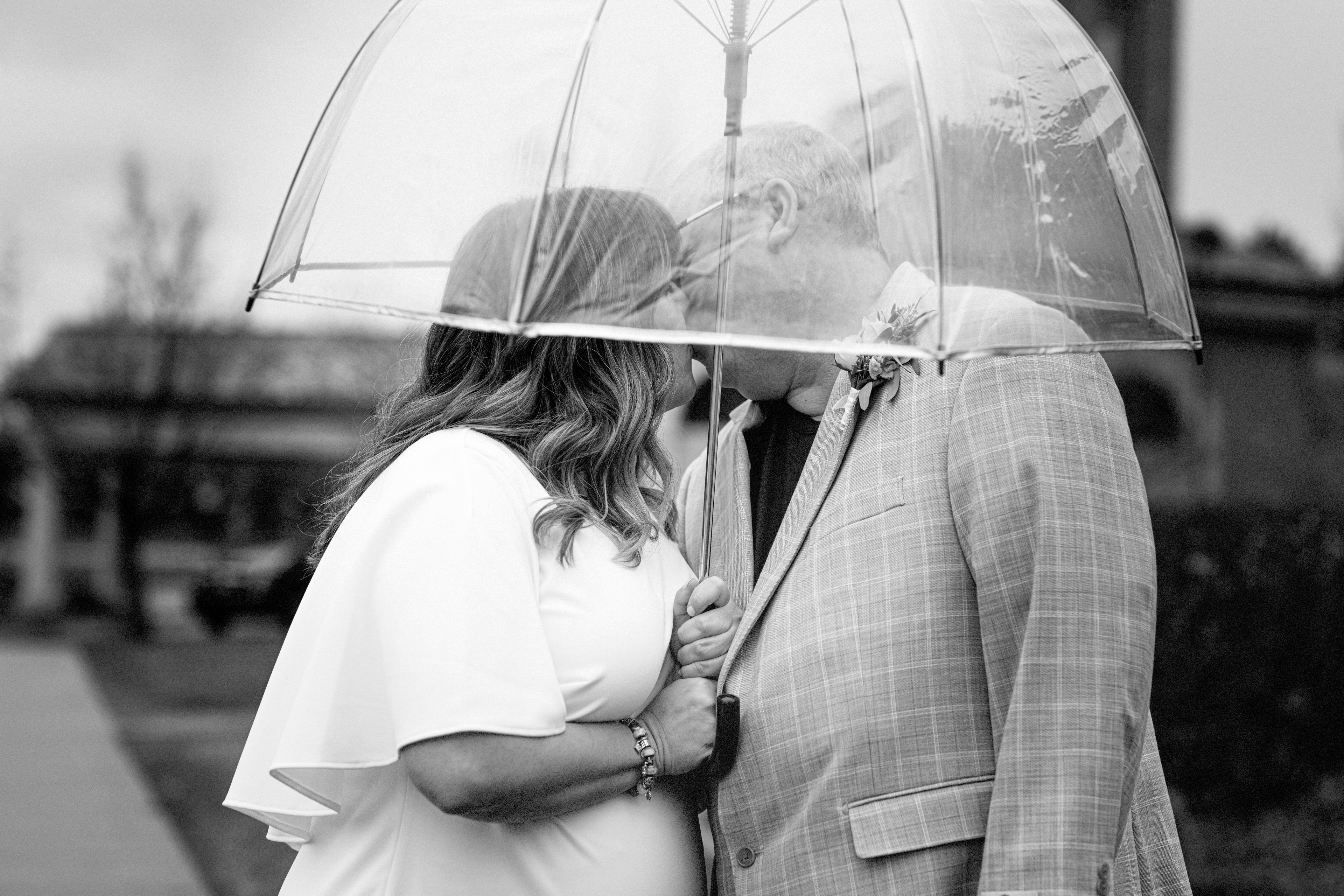 Couple kissing under clear umbrella in the rain — romantic wedding portrait